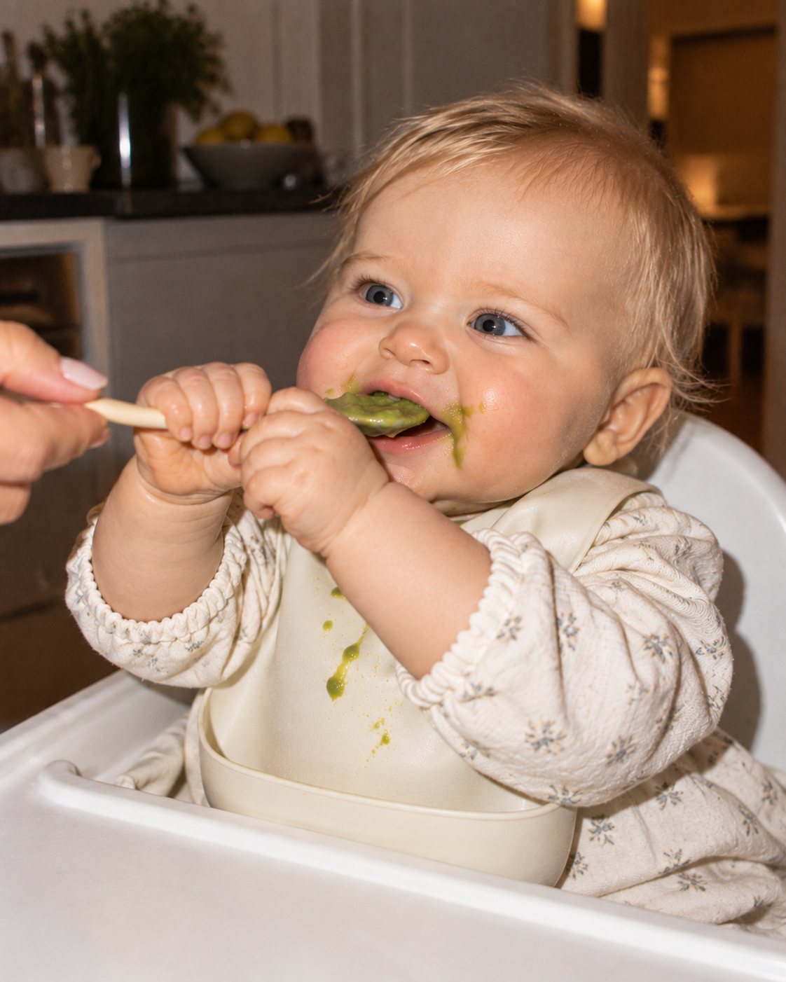 Baby in a high chair happily eating green purée from a spoon